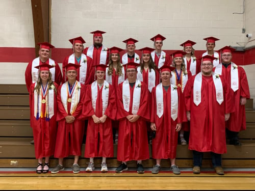 Class of 2021 in caps & gowns standing on bleachers in gym.