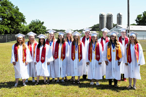 Class of 2020 standing outside on the ball field in their caps & gowns