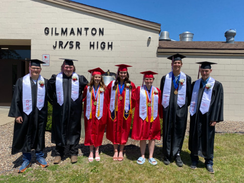 Class of 2023 in caps & gowns outside in front of high school building.